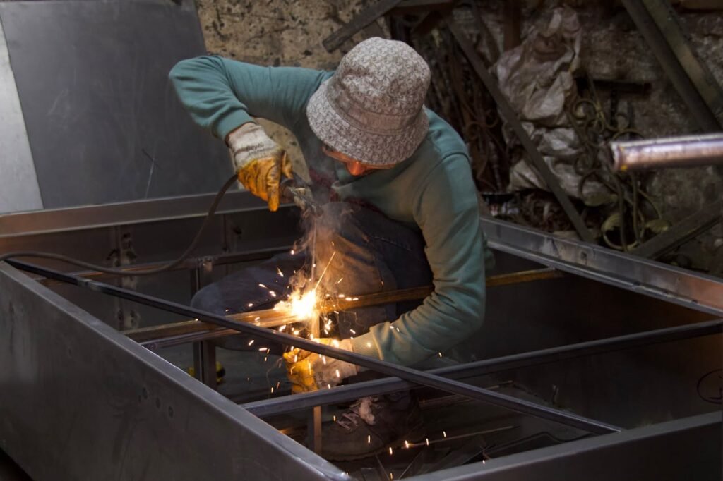 A metalworker uses a welding torch inside an industrial workshop, creating sparks.