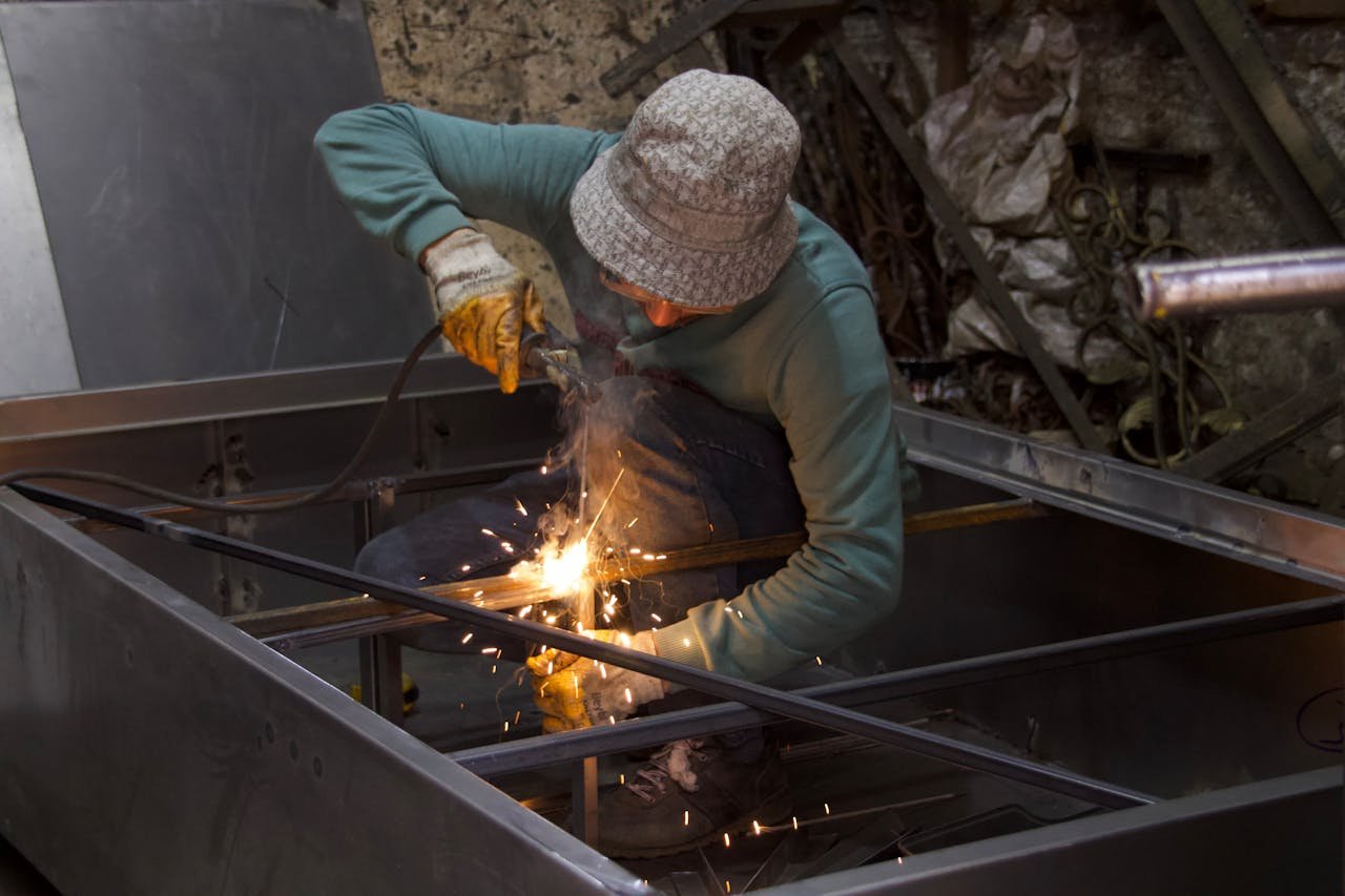 A metalworker uses a welding torch inside an industrial workshop, creating sparks.